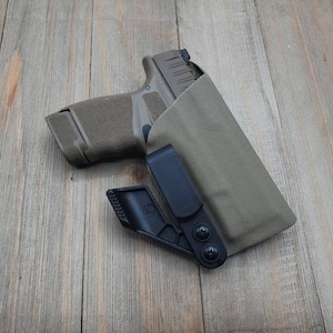 May include: A black and tan gun holster with a black clip and a gun inside. The holster is made of a soft material and has a smooth finish.