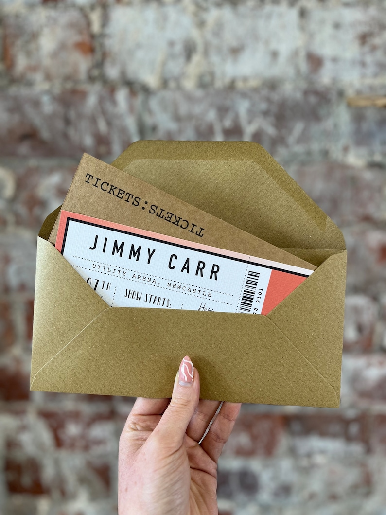 K&ouml;nnte beinhalten: Ein brauner Umschlag mit einem Ticket f&uuml;r eine Jimmy Carr-Show. Das Ticket ist wei&szlig; und korallenfarben mit schwarzem Text, einschlie&szlig;lich Veranstaltungsort und Datum. Der Umschlag wird vor einer Backsteinmauer gehalten.