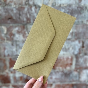 K&ouml;nnte beinhalten: Ein hellbrauner Kraftpapierumschlag, schr&auml;g gehalten, mit einer gefalteten Klappe. Der Umschlag hat eine strukturierte Oberfl&auml;che. Der Hintergrund ist eine Ziegelmauer.