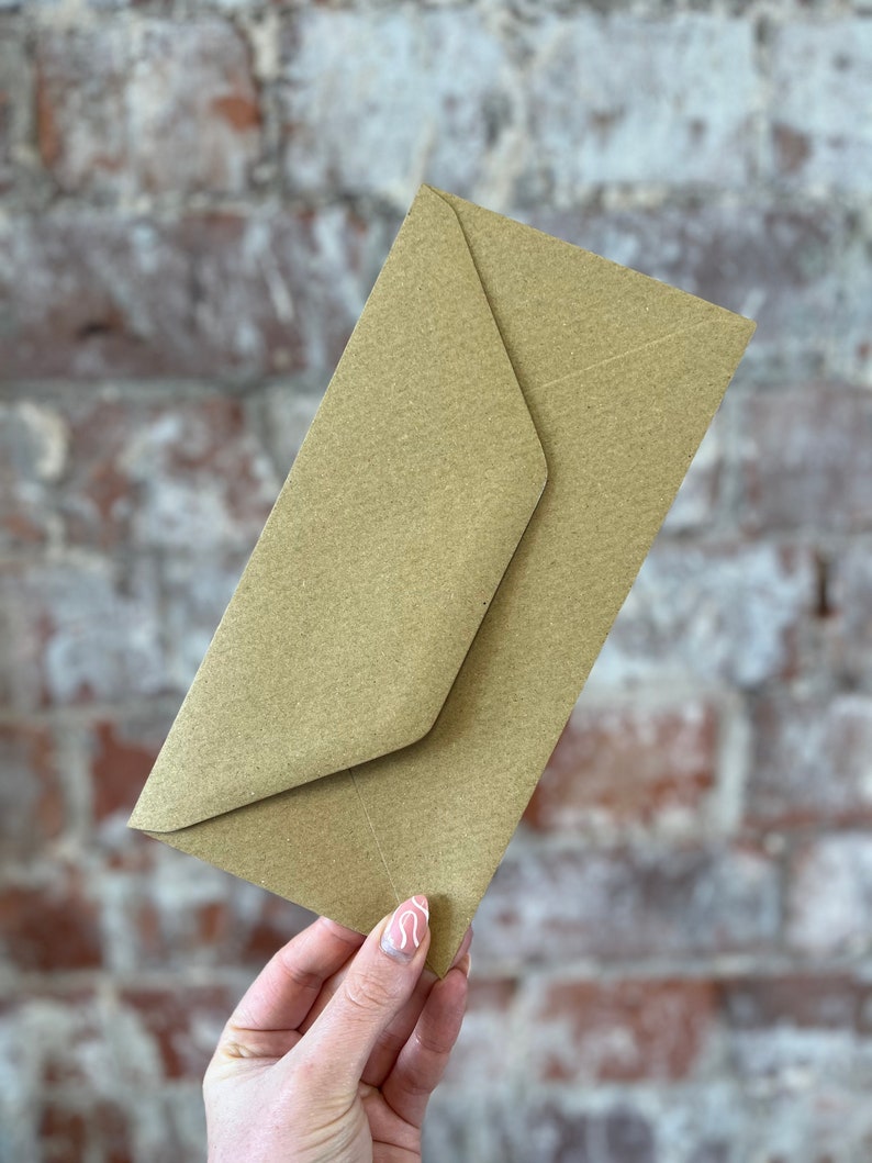 K&ouml;nnte beinhalten: Ein hellbrauner Kraftpapierumschlag, schr&auml;g gehalten, mit einer gefalteten Klappe. Der Umschlag hat eine strukturierte Oberfl&auml;che. Der Hintergrund ist eine Ziegelmauer.
