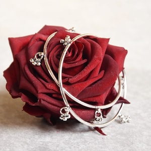 Peut inclure: Deux bracelets argentés avec des breloques pendantes, reposant sur une seule rose rouge.