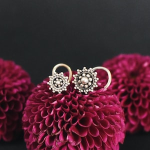 Peut inclure: Deux anneaux de nez en argent avec un design circulaire et de petites perles. Les anneaux sont placés sur trois boutons de fleurs roses.