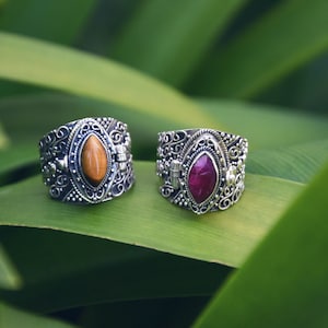 Peut inclure: Deux bagues en argent avec des motifs ornés et des incrustations de pierres précieuses. La bague de gauche a une pierre œil de tigre, tandis que la bague de droite a une pierre rubis.