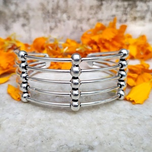 Peut inclure: Bracelet en argent avec cinq rangées de cercles reliés. Le bracelet est ouvert et a une forme arrondie.