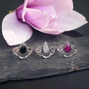 Op de afbeelding: Drie zilveren ringen met verschillende gekleurde edelstenen. De ringen hebben een traanvormige steen die is gezet in een halve maan ontwerp. De stenen zijn zwart, wit en rood.