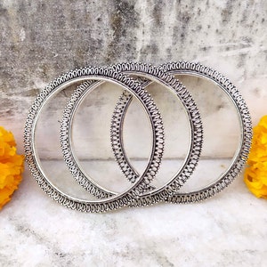 Peut inclure: Trois bracelets en argent avec des motifs délicats et complexes. Les bracelets sont empilés les uns sur les autres et ont une finition brillante.