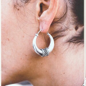 Peut inclure: Boucles d'oreilles créoles en argent avec un motif décoratif sur la bande.