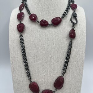May include: A long, layered necklace with a silver chain and large, dark red gemstone beads. The necklace has a lobster clasp closure.