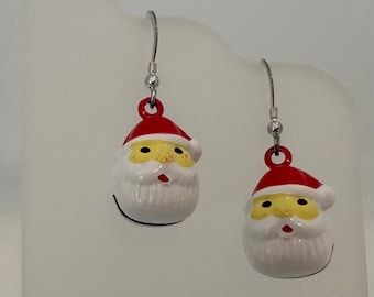 Puede incluir: Un par de pendientes de plata con forma de cara de Papá Noel en rojo y blanco. Las caras de Papá Noel tienen ojos amarillos y barbas blancas.