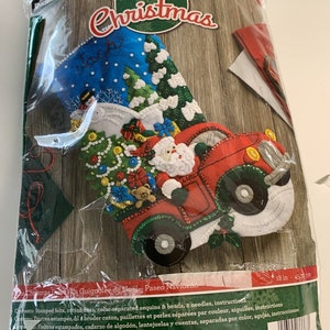May include: Felt Christmas stocking kit featuring a red truck carrying Santa Claus and a Christmas tree. The stocking is blue and white with the name "Jack" embroidered on it. The kit is 18 inches (45.72 cm) long.