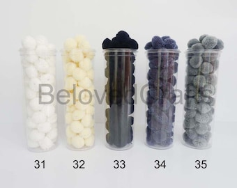 Può includere: Cinque barattoli trasparenti pieni di pon pon di vari colori. I barattoli sono etichettati da 31 a 35. I pon pon sono bianchi, crema, neri, blu scuro e grigi.