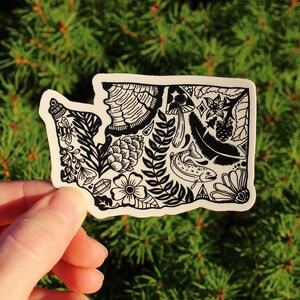 Puede incluir: Pegatina en blanco y negro del estado de Washington con una ilustraci&oacute;n detallada de diversas flora y fauna, incluyendo un pez, setas, bayas y pi&ntilde;as.