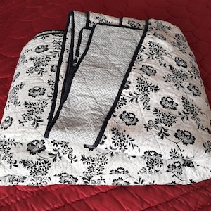 May include: A white and black floral patterned quilt with a navy blue border. The quilt is folded in half and is lying on a red surface.