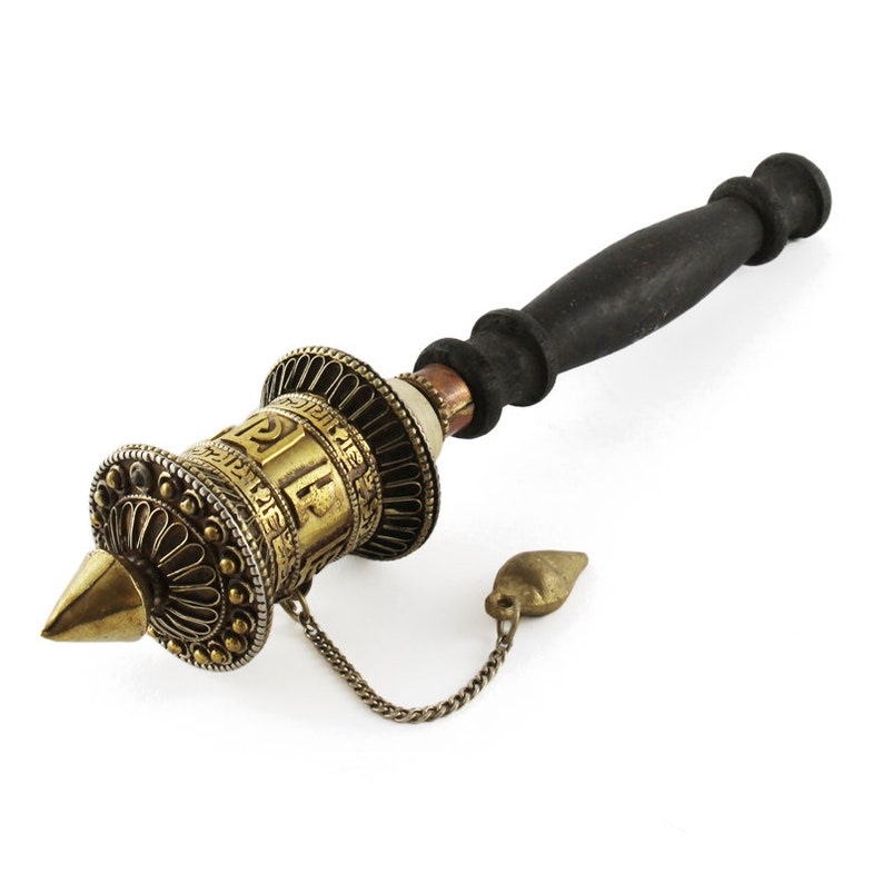 May include: A hand-held prayer wheel with a black wooden handle and a decorative brass cylinder. The cylinder features intricate patterns and inscriptions, with a conical tip and a small bell attached by a chain. The prayer wheel is a spiritual item.