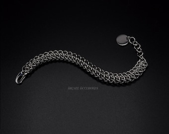 May include: A silver chain bracelet with a round, silver clasp. The bracelet is made of a woven chain pattern.