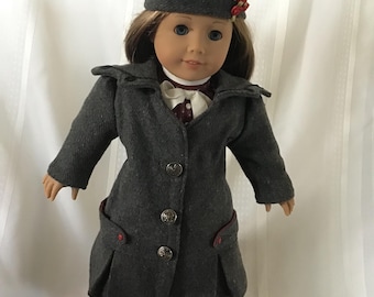 May include: A gray wool coat with red trim and buttons, worn by a doll with brown hair and a gray beret with a red flower accent. The doll is wearing a white blouse and a red and white plaid skirt.
