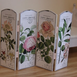 May include: A white wooden room divider with four panels. Each panel features a vintage postcard design with floral illustrations of roses and leaves. The text "Carte Postale" is printed on each panel.