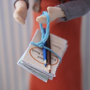 May include: A stack of small, cream-colored books tied together with a blue string. The books have the text "Excel" and "Cool Book" printed on the covers. Two wooden pencils are tucked into the string.