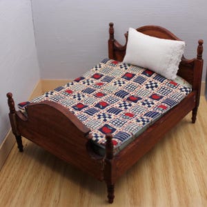May include: A miniature wooden bed frame with a dark brown finish, featuring four turned posts and a curved headboard. The bed is dressed with a quilt patterned in a grid of red apples and blue checkered squares, topped with a white lace-trimmed pillow.