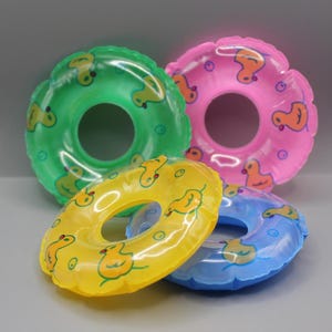 May include: Four colourful inflatable swim rings in green, pink, yellow, and blue. Each ring features a duck pattern. The rings are designed for water activities and are suitable for children.