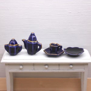 May include: A miniature dark blue ceramic tea set featuring a teapot, a lidded sugar bowl, a teacup on a hexagonal saucer, and a small scalloped plate. Each piece is finished with a thin gold trim along the edges and rims.