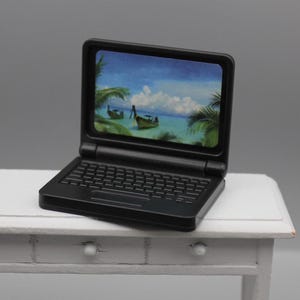 May include: A black laptop computer with a tropical beach scene on the screen. The laptop is sitting on a white table.