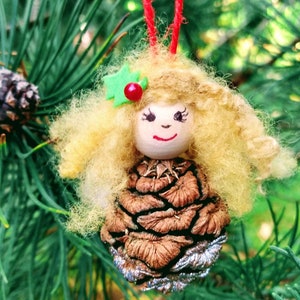 May include: A handmade Christmas bauble featuring a pine cone with a felt face and blonde hair. The bauble is decorated with a green felt leaf and a red felt berry.