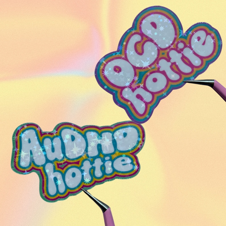 May include: Two stickers with the words "OCD hottie" and "AuDHD hottie" in a bubble font. The stickers have a white background with a star pattern and are outlined in a rainbow of colours. A pink tool holds each sticker.