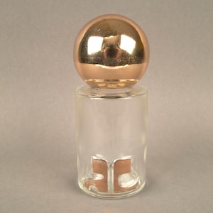 May include: A clear glass bottle with a copper colored sphere top and a copper colored letter 'B' on the front.