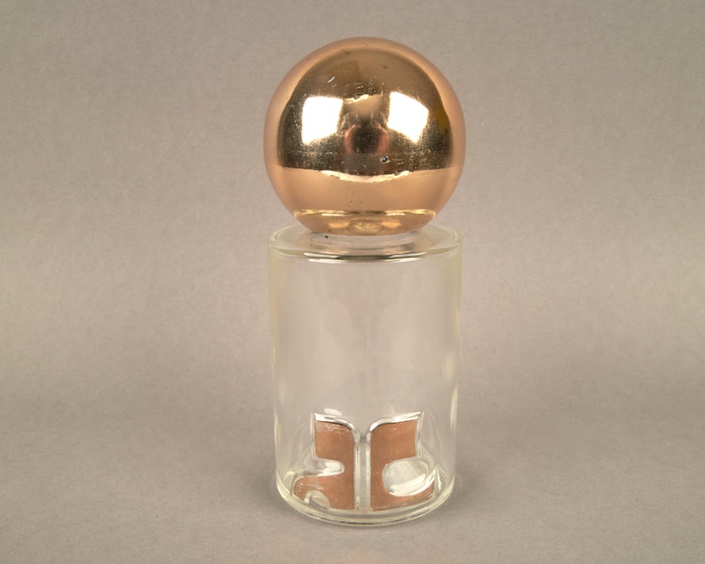 May include: A clear glass bottle with a copper colored sphere top and a copper colored letter 'B' on the front.