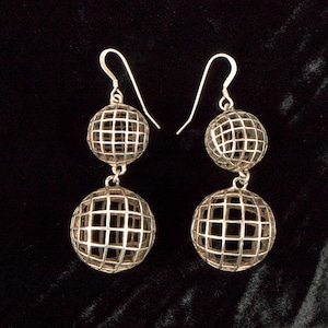 May include: A pair of silver-toned drop earrings. Each earring features two openwork spheres, one above the other, connected by a small chain. The spheres have a grid-like pattern, and the earrings hang from a simple hook.