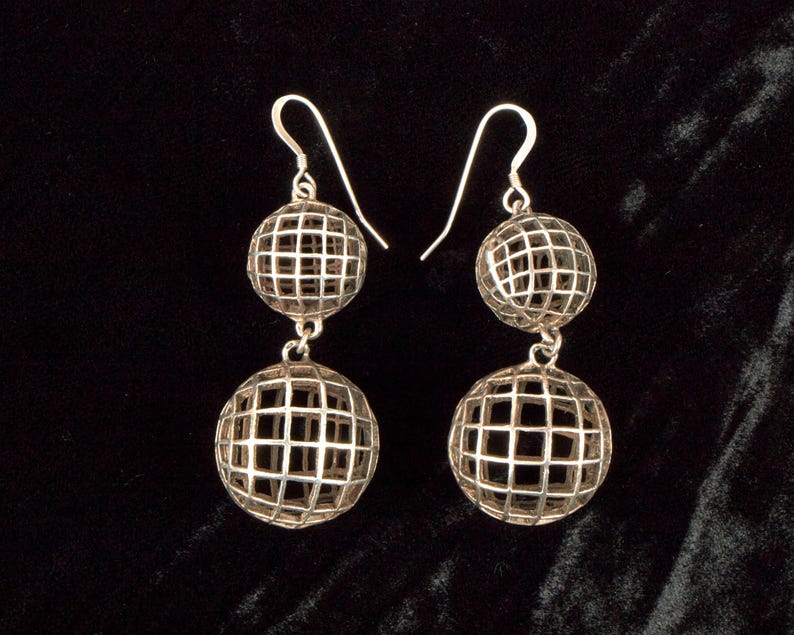 May include: A pair of silver-toned drop earrings. Each earring features two openwork spheres, one above the other, connected by a small chain. The spheres have a grid-like pattern, and the earrings hang from a simple hook.