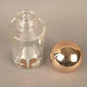 May include: A clear glass bottle with a gold stopper. The bottle has a gold label with the letters "SC" on it.