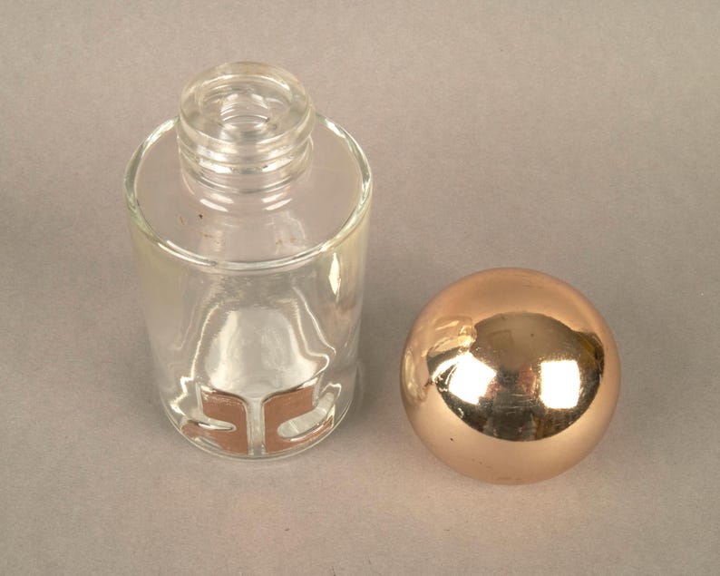 May include: A clear glass bottle with a gold stopper. The bottle has a gold label with the letters "SC" on it.