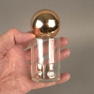 May include: A clear glass bottle with a gold ball stopper. The bottle has the number "25" embossed on the side.