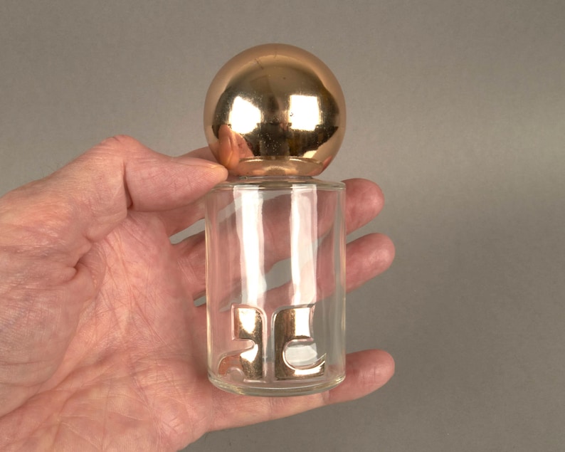 May include: A clear glass bottle with a gold ball stopper. The bottle has the number "25" embossed on the side.
