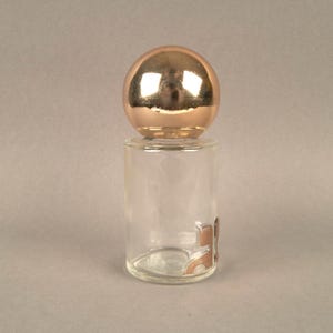 May include: A clear glass bottle with a gold-colored spherical stopper. The bottle has a textured surface and a gold-colored design on the bottom.