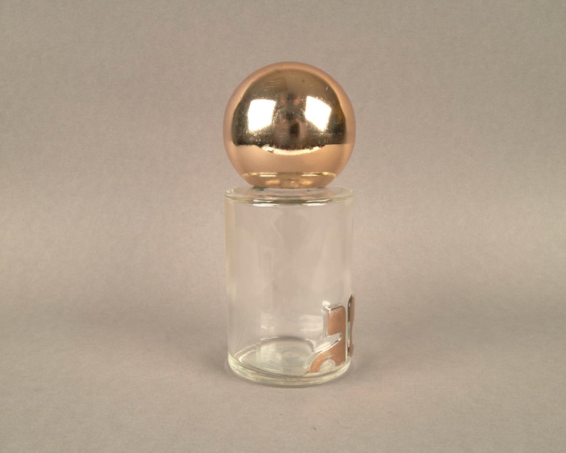 May include: A clear glass bottle with a gold-colored spherical stopper. The bottle has a textured surface and a gold-colored design on the bottom.