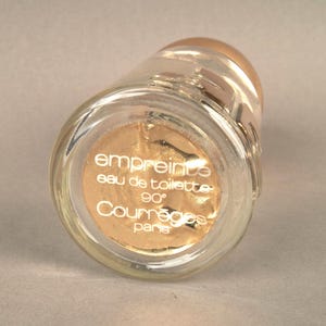 May include: A clear glass bottle with a gold label that reads "empreinte eau de toilette 90&deg; Courr&egrave;ges Paris".