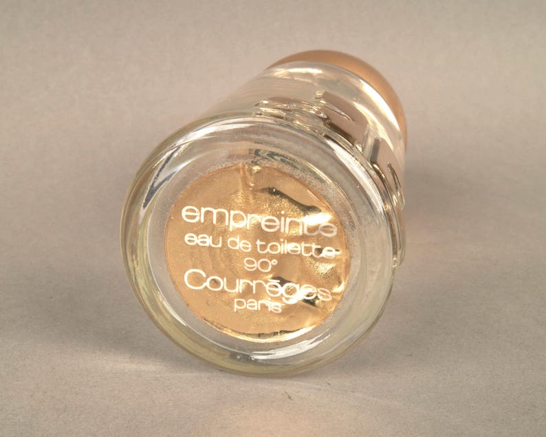 May include: A clear glass bottle with a gold label that reads "empreinte eau de toilette 90&deg; Courr&egrave;ges Paris".
