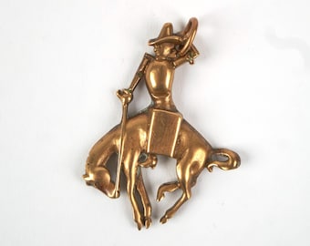 Colgante de latón vintage de los años 30 con figura de vaquero montando un caballo salvaje.