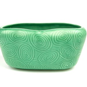 Peut inclure: Un pot de fleurs rectangulaire en céramique verte avec un motif de spirales répétées. Le pot a un bord supérieur légèrement incurvé et des coins arrondis. La surface a une finition brillante et la couleur est un vert moyen vif.