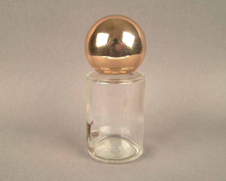 May include: A clear glass bottle with a gold-colored spherical stopper.