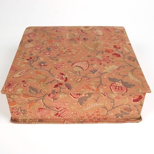 May include: A rectangular storage box covered in a fabric featuring a repeating floral and vine pattern in shades of muted orange, dusty pink, deep red, and soft green. The box has a flat lid and straight sides, with the fabric pattern aligned.