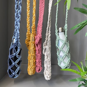 May include: Five crocheted bottle holders in different colours, including blue, yellow, pink, white, and green. Each holder is hanging from a cord and has a metal water bottle inside.
