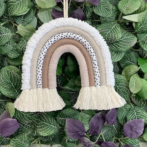 May include: A white, brown and black yarn rainbow wall hanging with a white pom-pom trim and fringe.