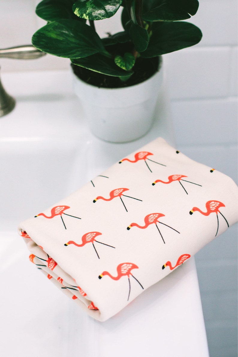 May include: A white hand towel with a pink flamingo pattern. The towel is folded and sitting on a white countertop.