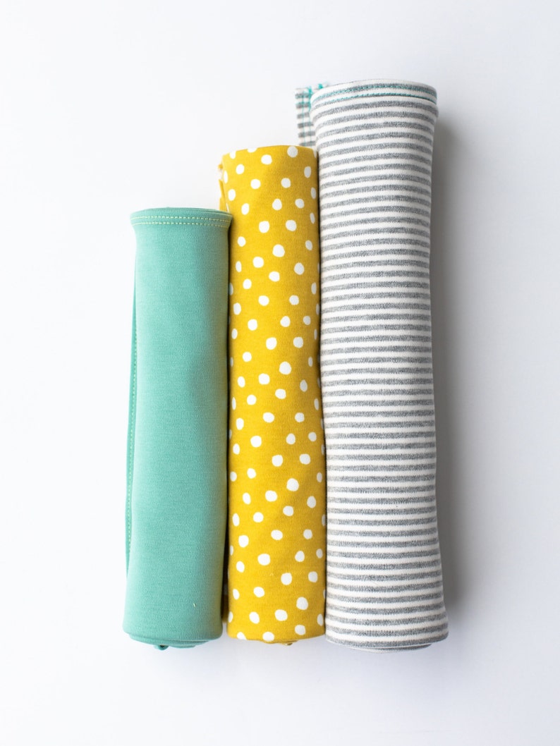 May include: Three rolled up fabric swatches. The first is a solid teal green, the second is yellow with white polka dots, and the third is grey with white stripes.