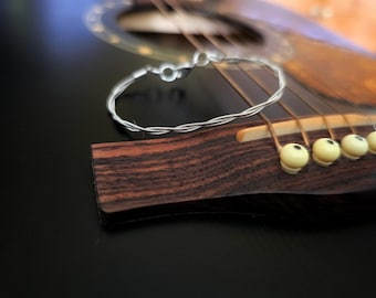 May include: Close-up of a wooden guitar bridge with a silver string wound around it. The bridge has six white tuning pegs.