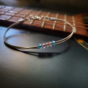 Peut inclure: Un bracelet en corde de guitare argenté avec des perles bleues et roses.